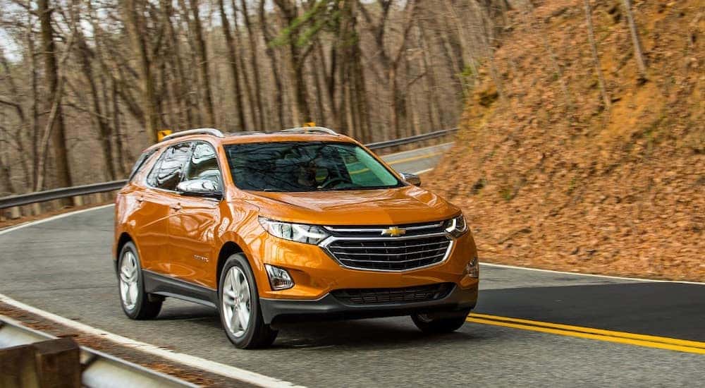 Orange 2019 Chevrolet Equinox SUV driving down a paved road next to trees and a hill