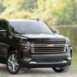 Black 2021 Chevrolet Tahoe High Country SUV parked on a dirt and grass path next to water