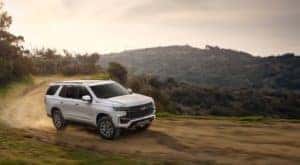 White 2021 Chevrolet Tahoe SUV driving on a dirt road near a cliff with mountains in the distance