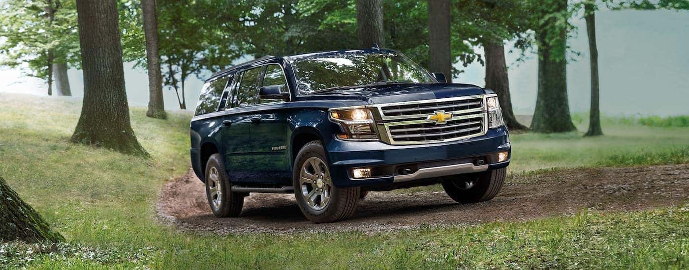 A blue 2020 Chevy Suburban is driving on a dirt trail in the woods.