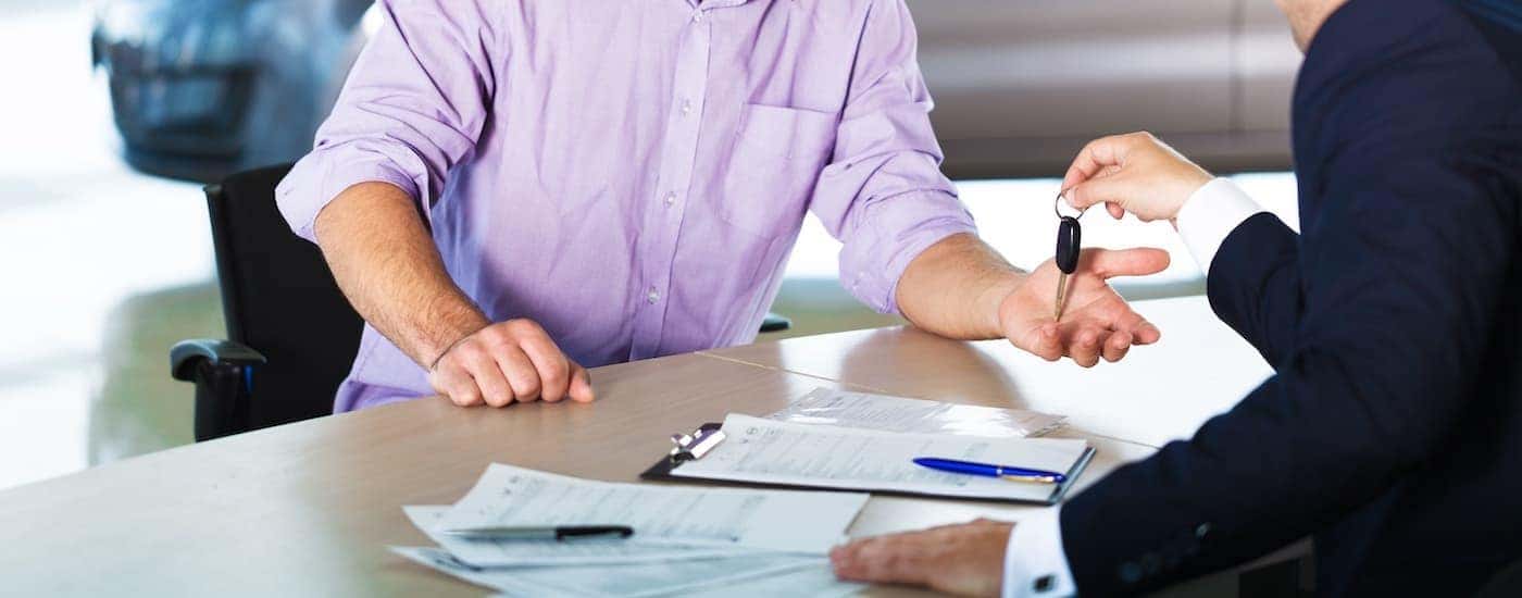 A salesman is handing keys to a customer after filling out the finance paperwork.