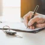 A hand completing paperwork for buying and registering a car.