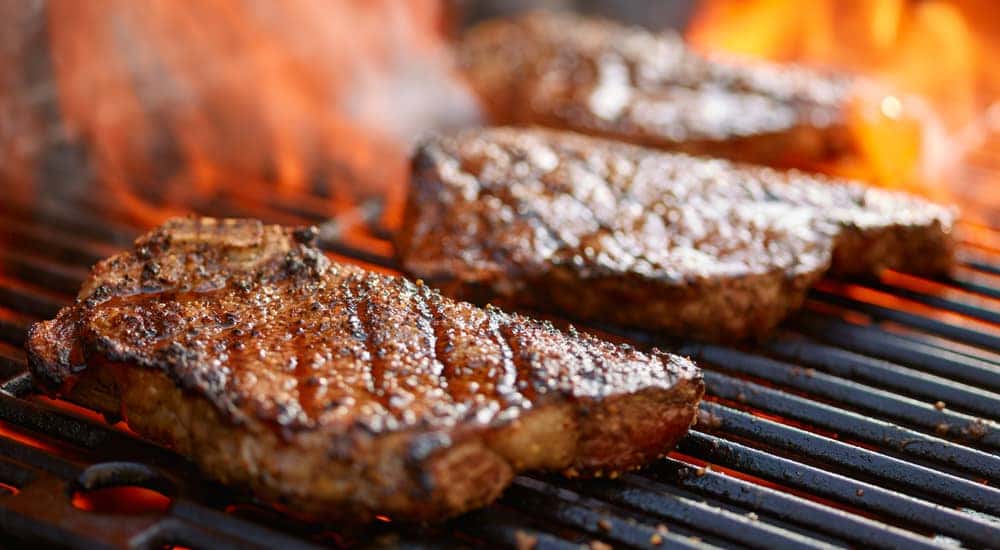 Three steaks sitting on a grill with flames coming through