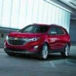 A red 2019 Chevy Equinox, which is popular among used cars in Albany, NY, is driving past a bright city building at night.
