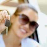 A woman is out of focus while she holds a car key in front of her.