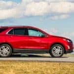 Red 2020 Chevrolet Equinox driving down a paved road next to green grass in front of a blue sky