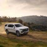 White 2021 Chevrolet Tahoe driving down a dirt road next to a cliff with mountains and trees in the background