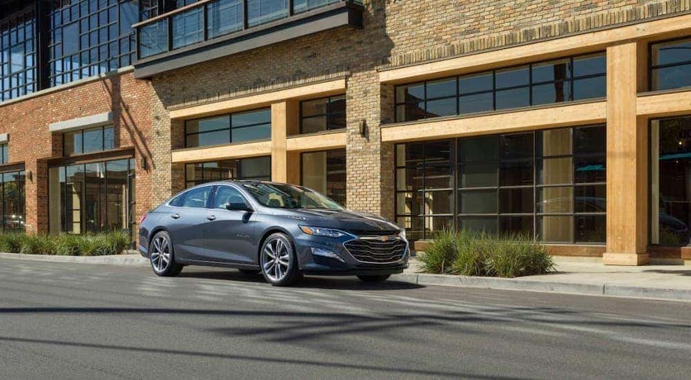 One of the many Chevy cars available at your local Albany dealer, a gray 2020 Chevy Malibu is shown driving on a street.