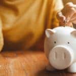 Woman in a yellow shirt putting a coin into a white piggybank