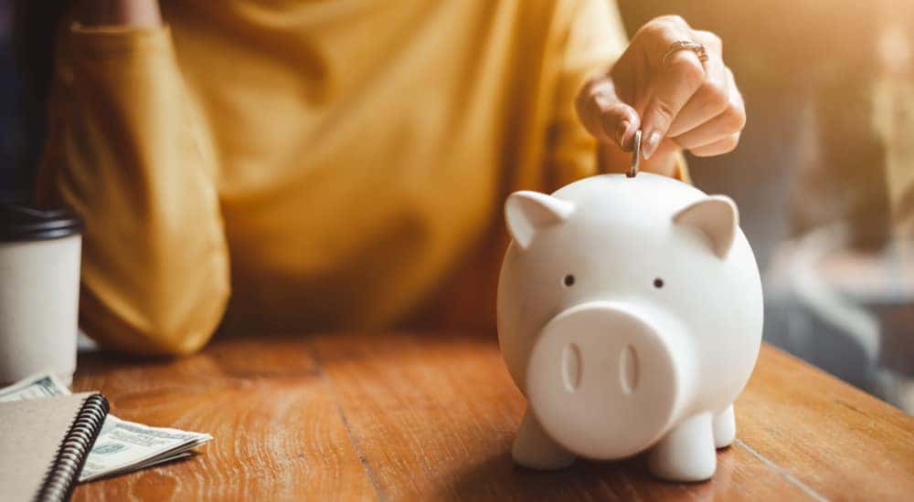 Woman in a yellow shirt putting a coin into a white piggybank