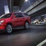 A red 2021 Chevy Tahoe RST is driving under an Albany, NY, bridge at night.