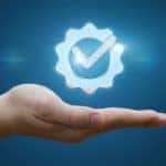 Man's hand below a floating and glowing blue gear and checkmark logo