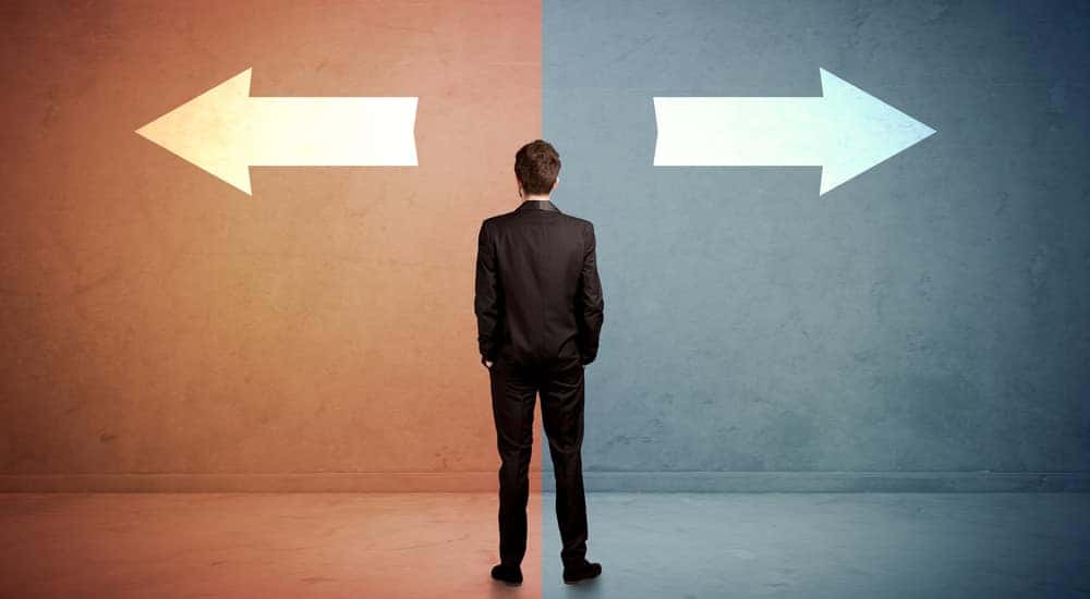 Man in a black suit standing in front of a half orange, half blue wall with arrows facing in opposite directions
