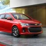 A popular car for sale near you, a red 2020 Chevy Sonic Hatchback, is parked in front of a modern home.