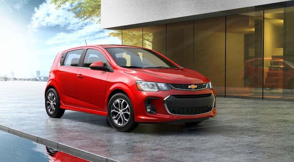 A popular car for sale near you, a red 2020 Chevy Sonic Hatchback, is parked in front of a modern home.