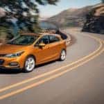 An orange 2018 Chevy Cruze Hatchback is driving along a winding road.