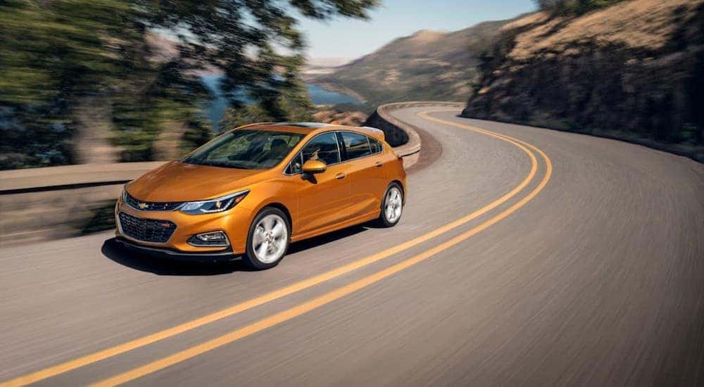 An orange 2018 Chevy Cruze Hatchback is driving along a winding road.