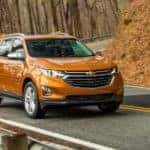 An orange 2020 Chevy Equinox is driving on a winding road in the fall.