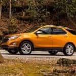 An orange 2019 certified pre-owned Chevy Equinox is driving on a rural road around Albany, NY, in the fall.