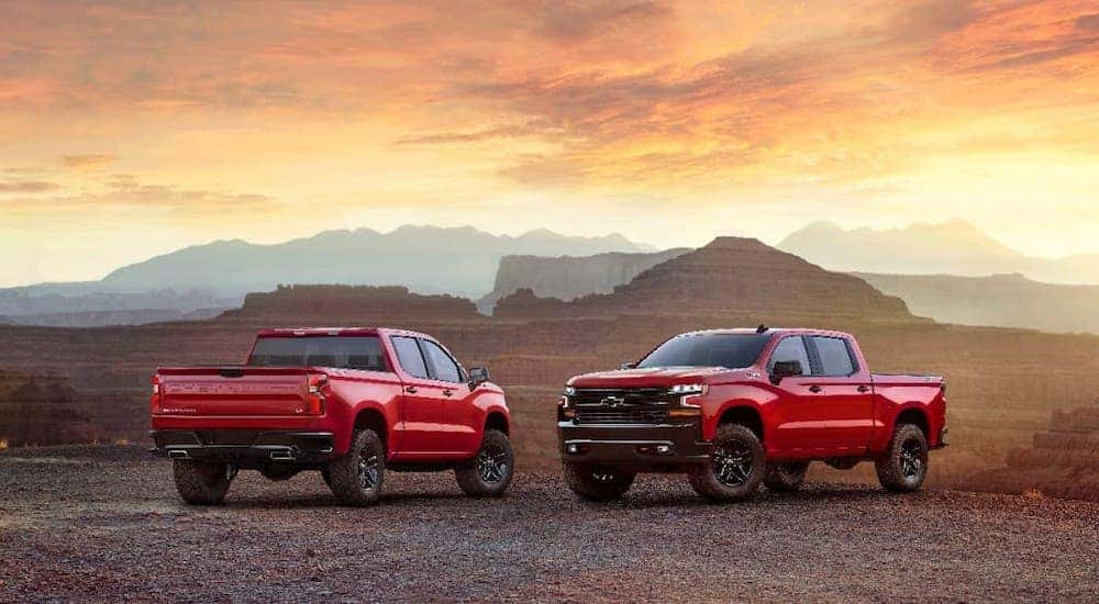 Two red 2019 Chevy Silverado trucks are parked in front of a canyon at sunset.