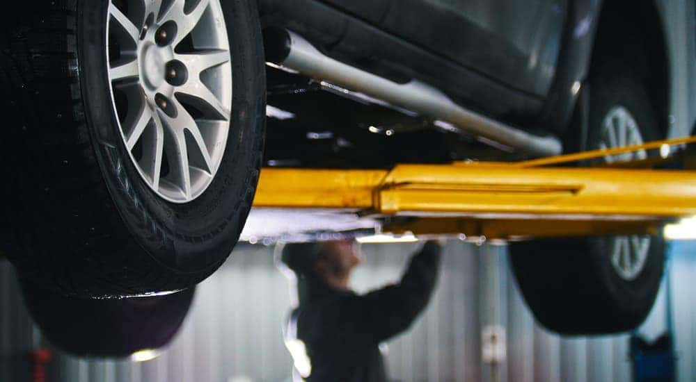 A mechanic is working under a car on a lift.