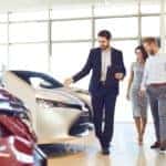 A salesman is showing a couple certified pre-owned cars in a dealership near Albany, NY.