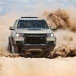 A tan 2021 Chevy Colorado ZR2 from a Chevy dealership near Clifton Park, NY, is kicking up sand and shown from the front.
