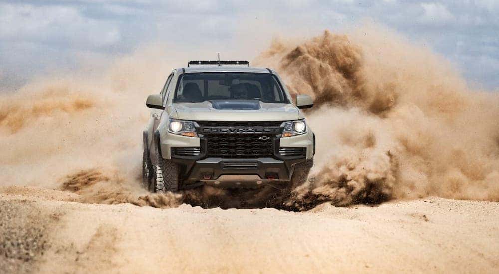 A tan 2021 Chevy Colorado ZR2 from a Chevy dealership near Clifton Park, NY, is kicking up sand and shown from the front.