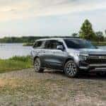 A gray 2021 Chevy Suburban Z71 from a Chevy dealership near Clifton Park, NY, is parked in front of a pond.