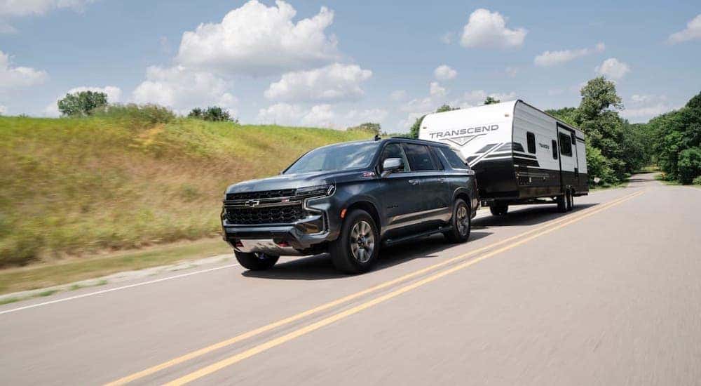A gray 2021 Chevy Suburban is towing a camper trailer on a road near Clifton Park, NY.