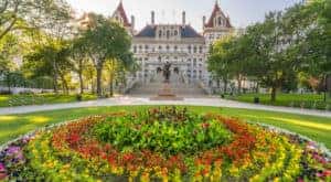 Circular bed of flowers in front of the tall, stone, New York state building in Albany