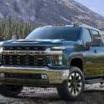 Blue 2020 Chevrolet Silverado 2500HD parked on rocks in front of tall trees and mountains