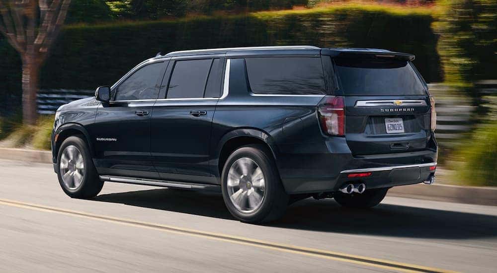A dark blue 2021 Chevy Suburban is driving past a fence and hedges.