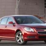 Red 2010 Chevrolet Malibu sedan parked in front of a cement building