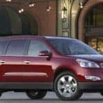 Maroon 2011 Chevrolet Traverse parked in front of a tall brick building and underneath lights