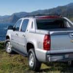 Back to front view of silver 2013 Chevrolet Avalanche in front of mountains