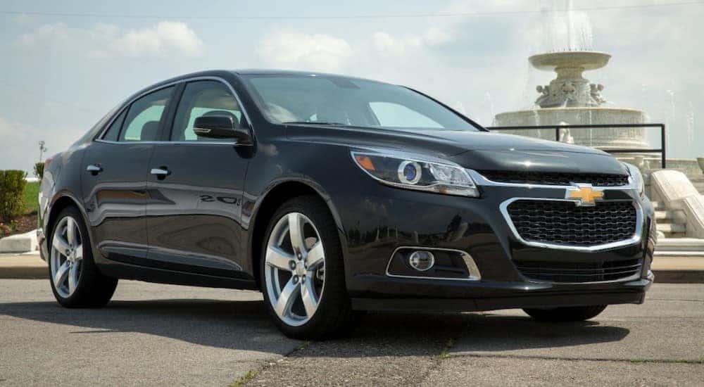 Front angled view of a black 2014 Chevrolet Malibu sedan parked in front of a cement fountain