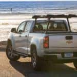 Back to front view of a silver 2015 Chevrolet Colorado pickup truck parked in front of the ocean