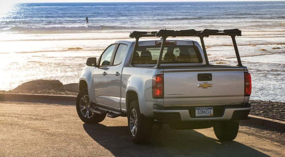 Back to front view of a silver 2015 Chevrolet Colorado pickup truck parked in front of the ocean