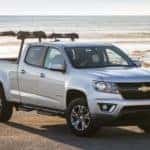 Silver 2015 Chevrolet Colorado with a truck rack on it parked in front of a body of water