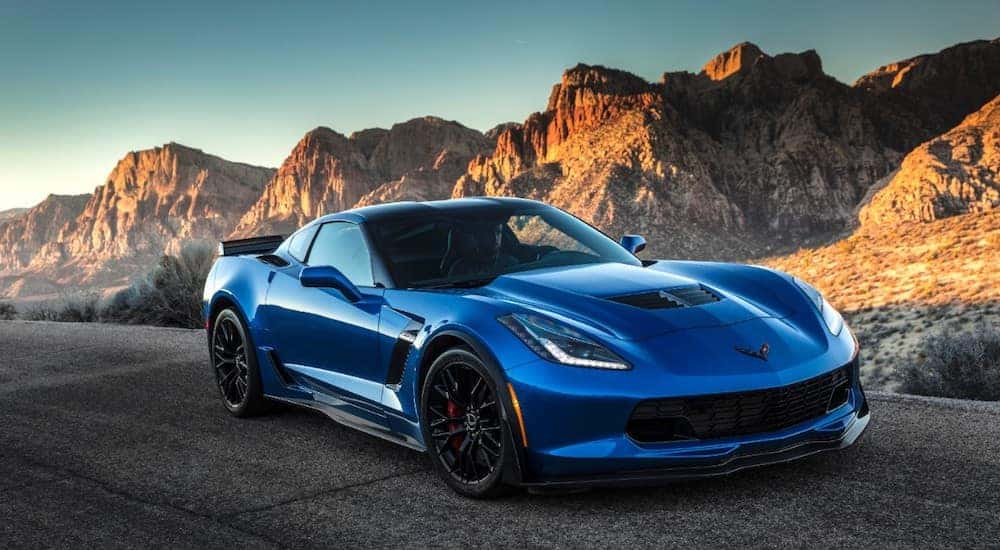 Angled view of a blue 2015 Corvette Z06 driving on a paved road next to rocky hills