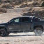 Black 2016 Chevrolet Colorado driving down a dirt road with shrubs and a hill in the background