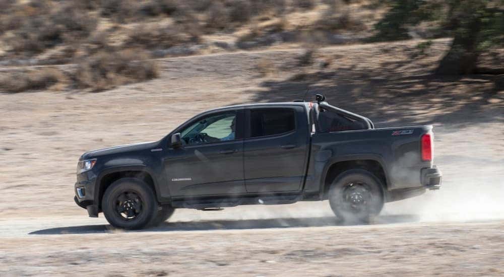 Black 2016 Chevrolet Colorado driving down a dirt road with shrubs and a hill in the background