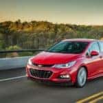 Red 2016 Chevrolet Cruze sedan driving down a paved road next to a guardrail and trees