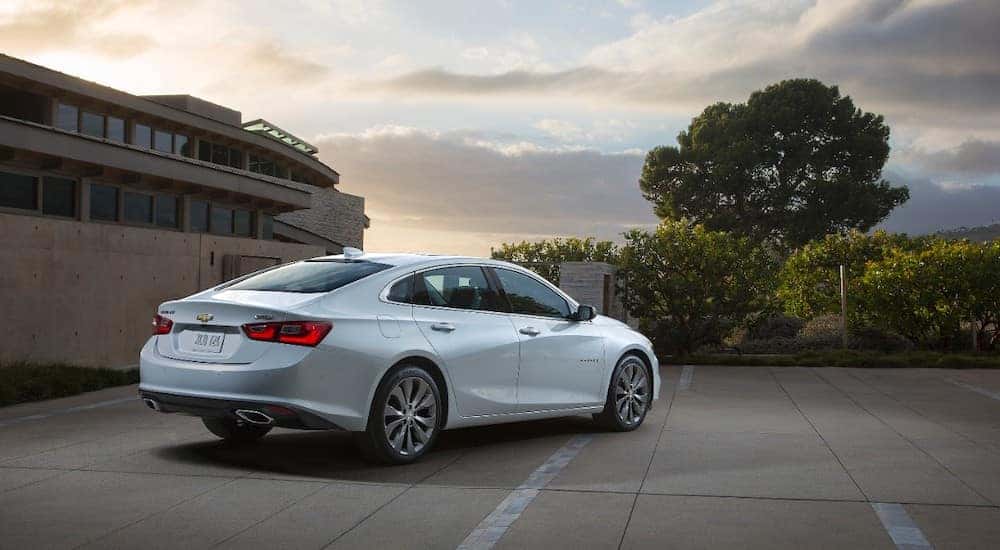 2016 Chevrolet Malibu sedan parked in a parking lot next to a brown building, facing green trees