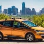 Award winning orange 2017 Bolt EV parked in front of trees and a city skyline