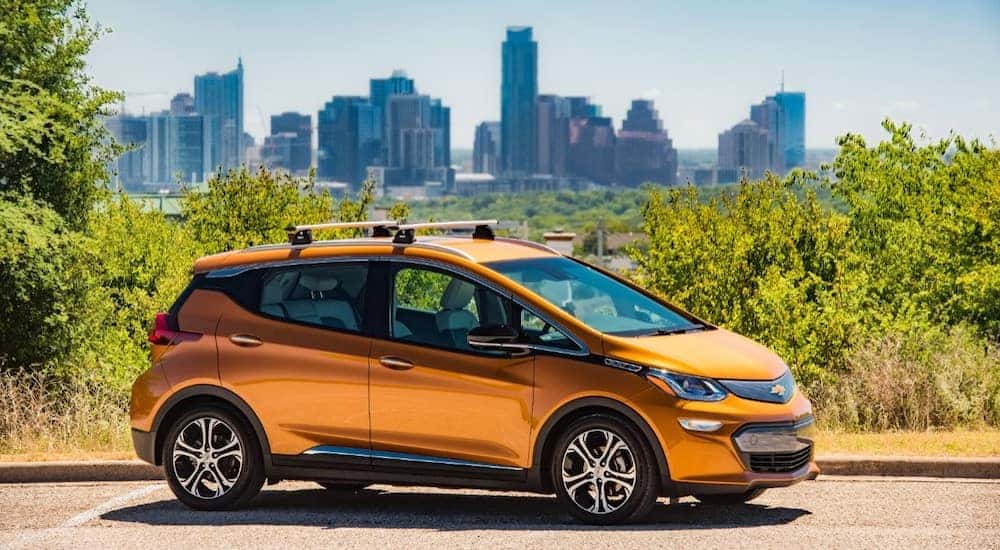 Award winning orange 2017 Bolt EV parked in front of trees and a city skyline