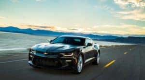 Black 2017 Chevrolet Camaro driving down a paved road next to a body of water and mountains