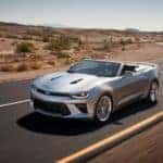 Silver 2017 Chevy Camaro SS convertible driving down a paved road with dirt and plants on either side