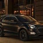 Black 2017 Chevrolet Equinox SUV parked in front of a brick building with strings of lights in the windows